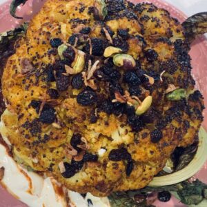 Whole roasted Indian spiced cauliflower topped with currants, pistachios and mustard seeds on yoghurt