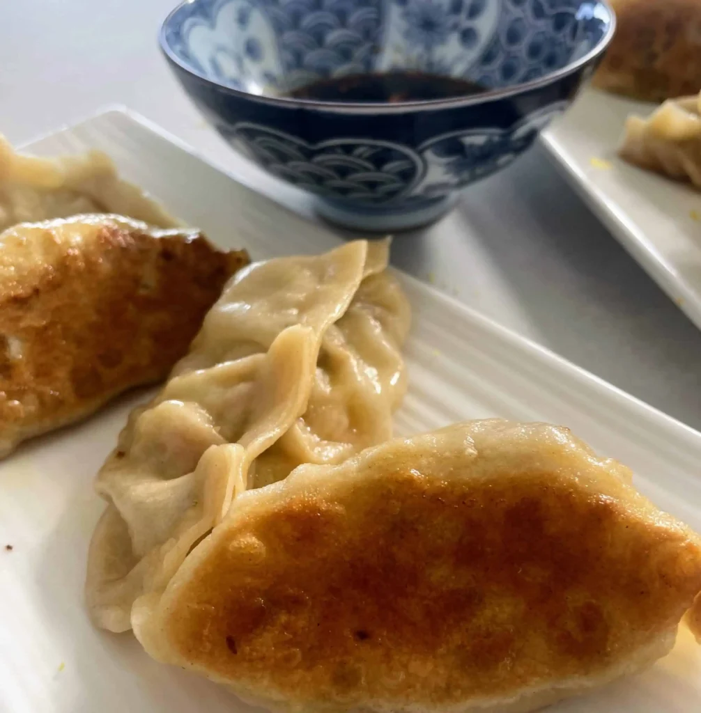 Pan fried dumplings made with hot water dough wrappers, with a bowl of soy dipping sauce