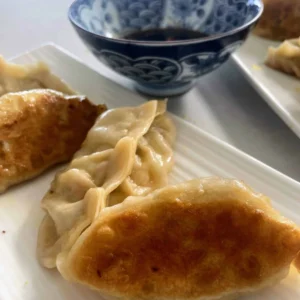 Pan fried dumplings made with hot water dough wrappers, with a bowl of soy dipping sauce