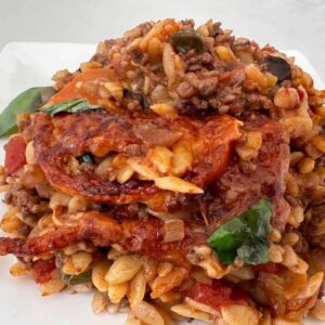 Baked puttanesca pasta with beef, olives, melted cheese and fresh basil on a white plate
