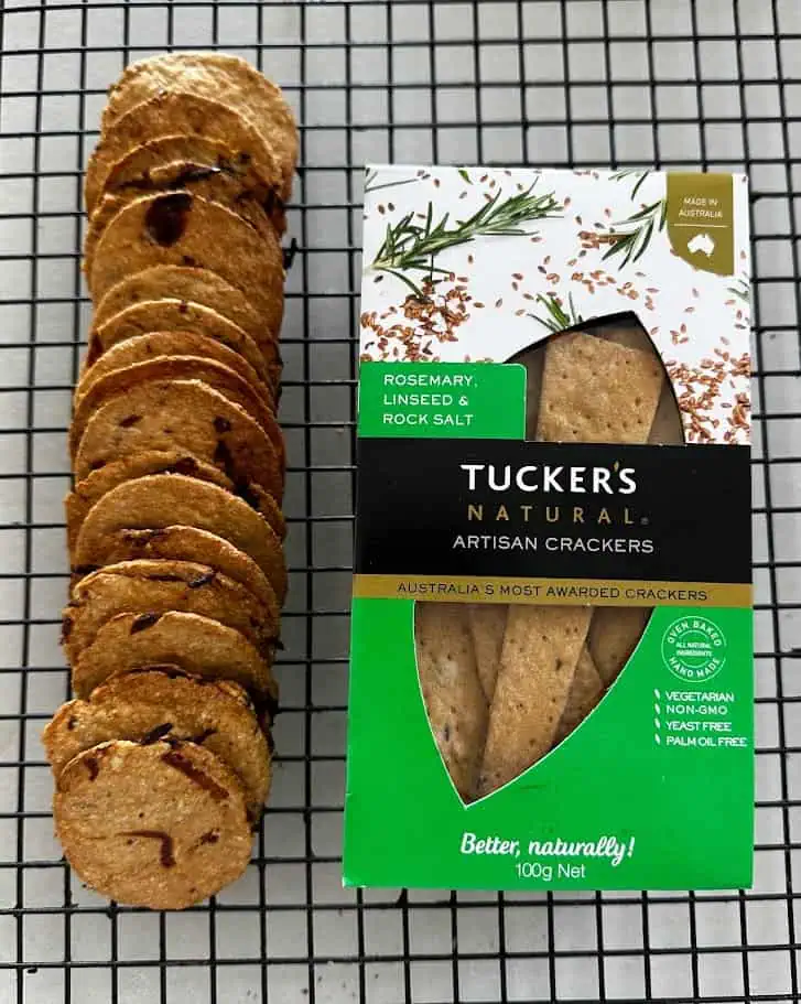 Homemade miso caramelised onion crackers cooling on a wire rack beside a box of Tuckers Natural artisan crackers