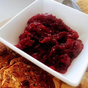 Glossy spiced beetroot relish in a white square dish beside seeded crackers