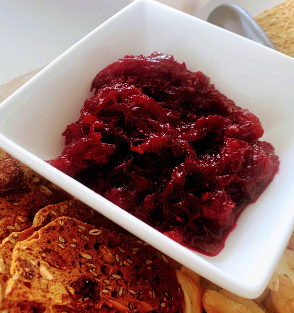 Glossy spiced beetroot relish in a white square dish beside seeded crackers