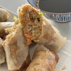 Crispy Thai inspired spring rolls cut open to show the pork and vegetable filling, with a bowl of dipping sauce