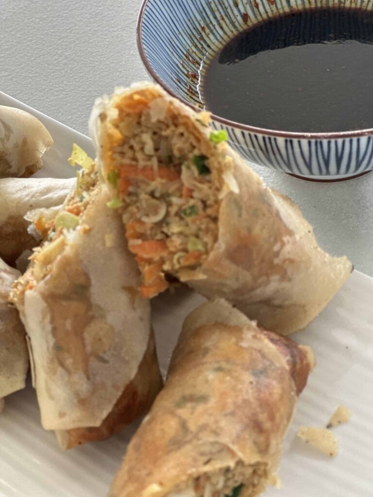 Crispy Thai inspired spring rolls cut open to show the pork and vegetable filling, with a bowl of dipping sauce