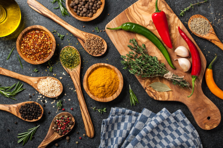 Bowls and spoons of whole spices, dried chilli, turmeric and fresh herbs laid out ready to pound into curry paste