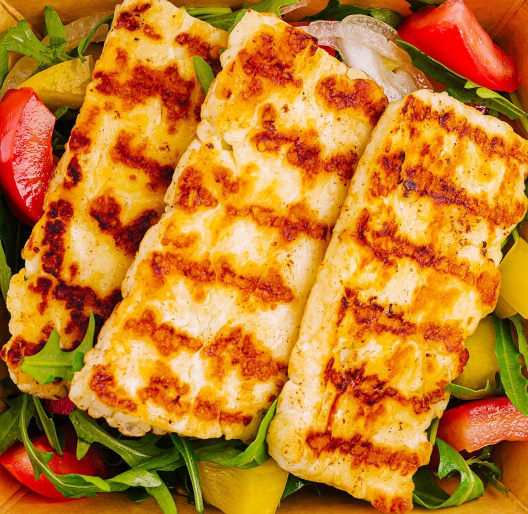 Slices of grilled haloumi served over a fresh salad with roast vegetables and rocket