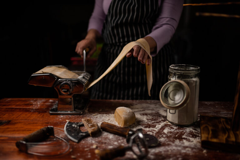 Hands working fresh pasta dough on a bench during a pasta class